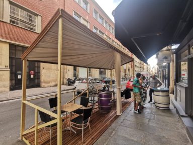 Terrasse de café avec tables, chaises et clients sur une rue animée.